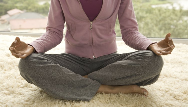 A woman meditating on a rug in front of a window.