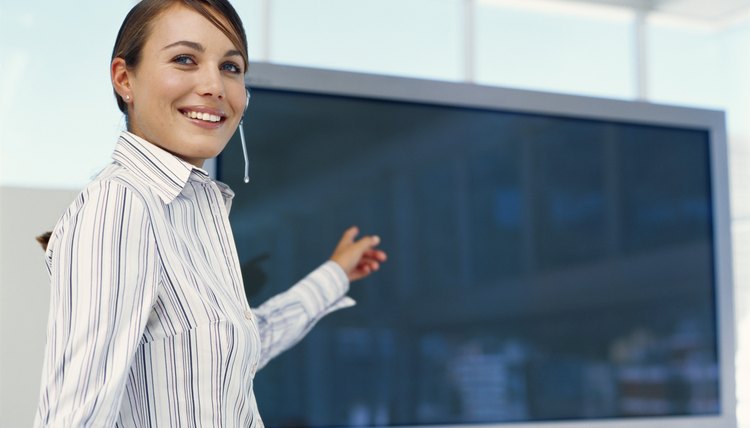 Businesswoman giving presentation at seminar, pointing at flat screen, side view