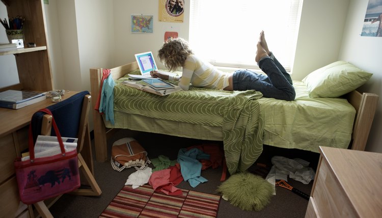 A young woman is lying on her bed in her dorm room.