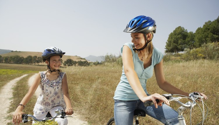 Mother and daughter (9-11) cycling, smiling at each other