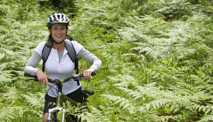 Portrait of mid adult woman standing amongst ferns with mountain bike, smiling