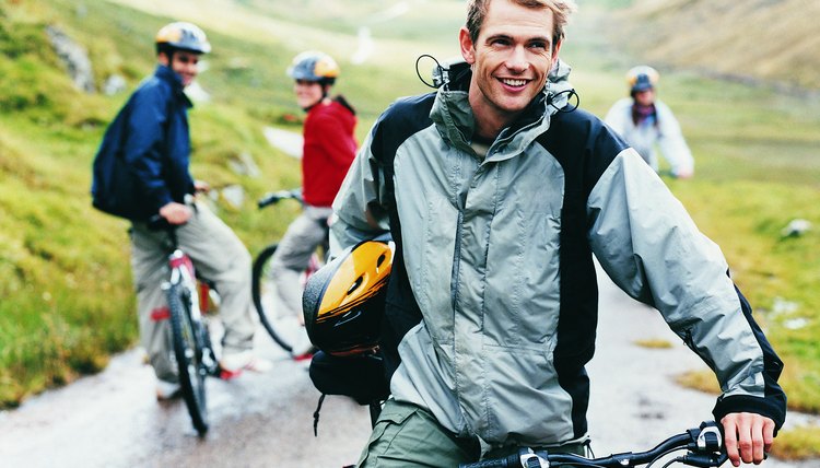 Young Man Stands Holding his Mountain Bike While his Three Friends Wait for him in the Background