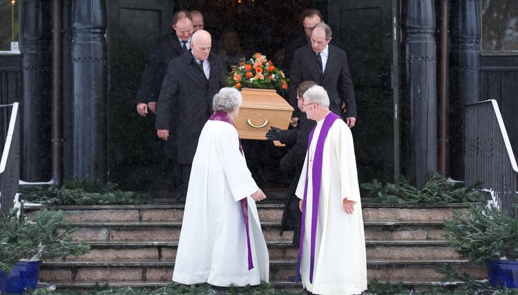 Pallbearers carrying a coffin down the steps of a church.