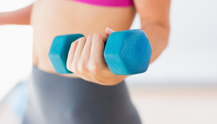 Mid section of a woman lifting dumbbell weight in gym