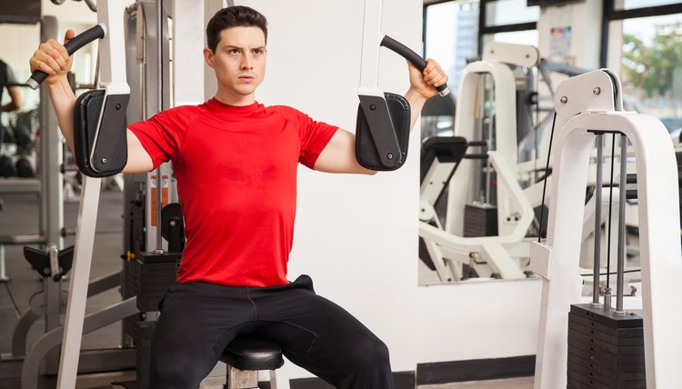 Handsome young man using the pec deck machine to work on his muscles at the gym