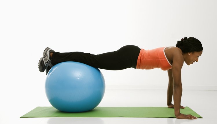 Profile of African American woman doing push ups with feet on exercise ball.