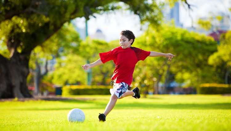 Young excited boy kicking ball in the grass