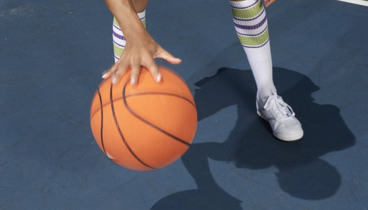 Woman standing dribbling basketball, low section, blurred motion