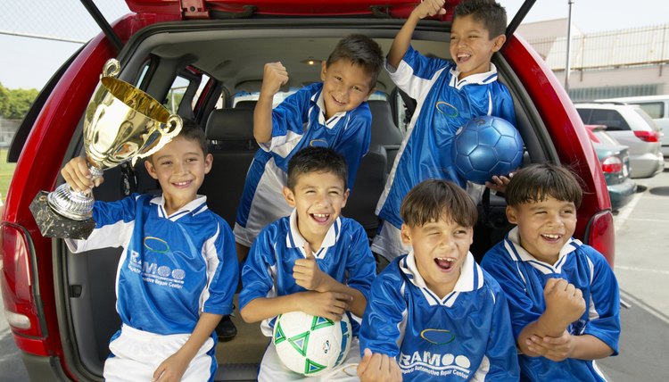 Boys (7-11) football team in car boot, holding trophy, smiling