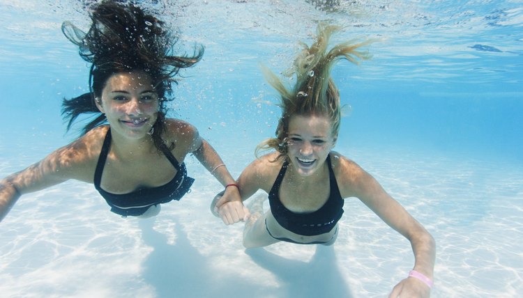 underwater lifestyle shot of two teenage female friends as they swim together in a pool