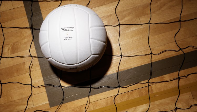 Volleyball and net on hardwood floor of volleyball court