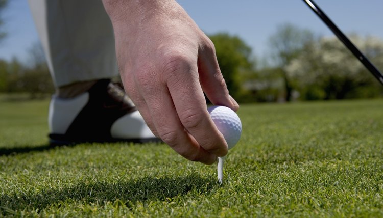 Close-up of a young man putting a golf ball on a tee