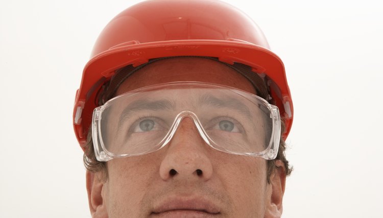 Man wearing protective eyewear and hard hat, looking up