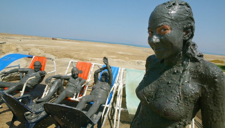 Tourists covered in mineral mud at spa resort on the Dead Sea shoreline