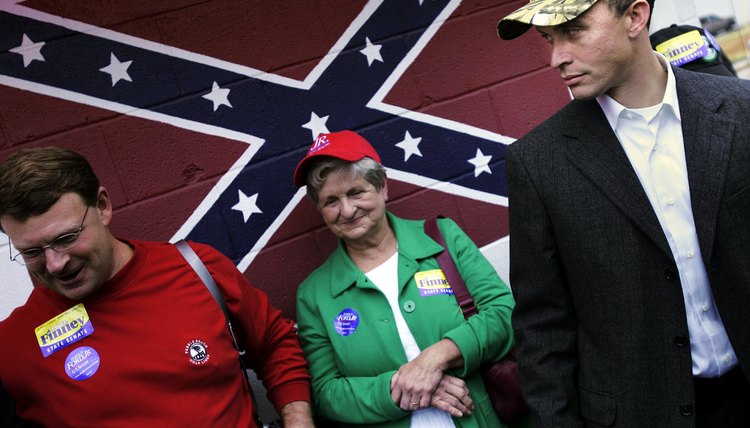 A woman is standing in front of a Confederate flag.