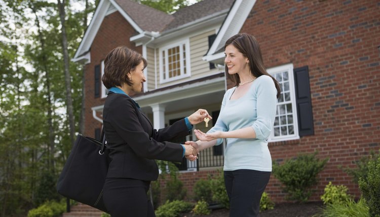 Un asesor inmobiliario entrega llaves a una mujer afuera de una casa.