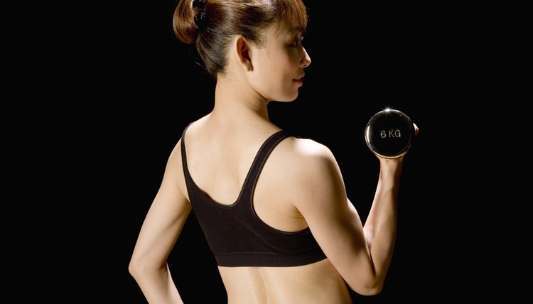 Woman lifting dumbbell, stretching, rear view, black background