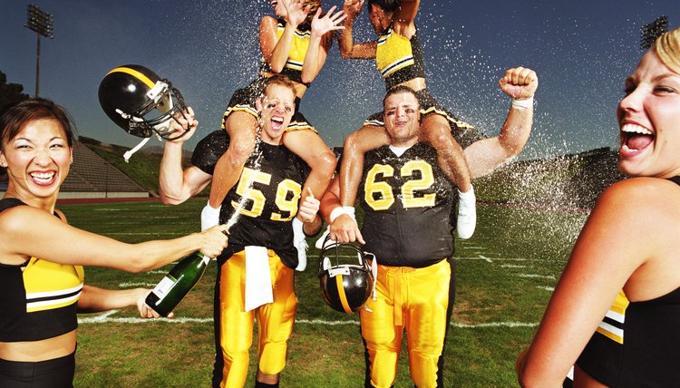 Two football players with cheerleaders, being sprayed with champagne