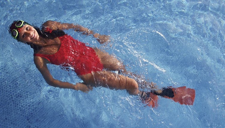 Young woman, swimming on back,  wearing goggles and flippers, in swimming pool,  portrait