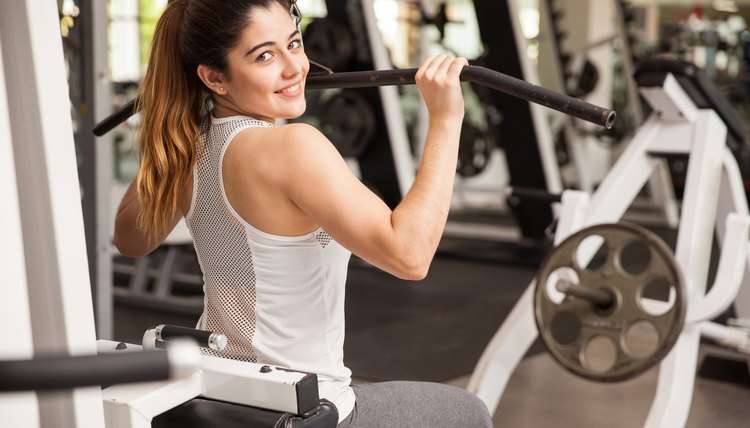 Beautiful Hispanic young woman working out on a pull down machine at the gym