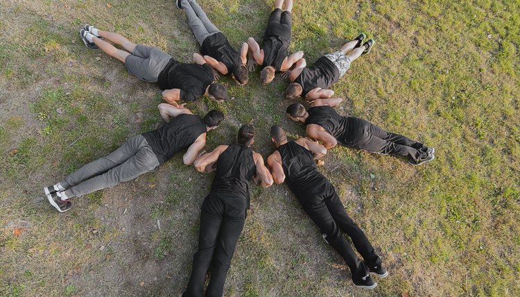 Group of fitness people doing push ups in park.