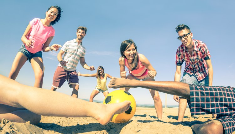 Group of multiracial friends playing beach soccer