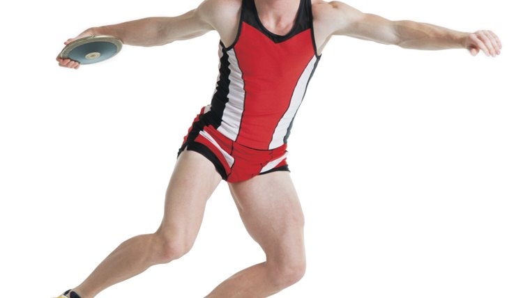 a young caucasian man wearing a red track uniform is preparing to throw a discus as he spins on one foot