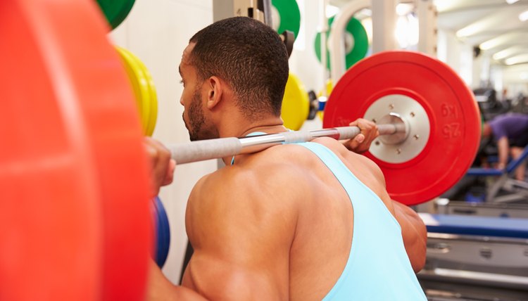 Man weightlifting barbells at a squat rack in a gym
