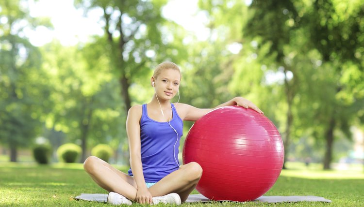 Young female in sportswear sitting on grass with pilates ball