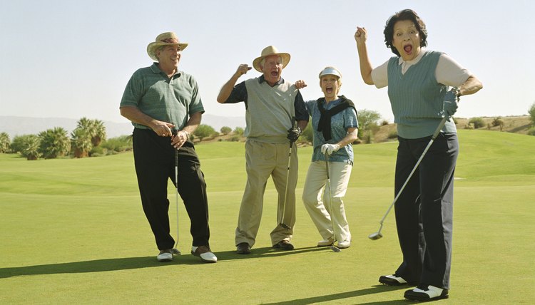 Four mature golfers standing on golf course, cheering