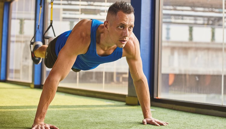 Young male fitness model training at the gym with trx