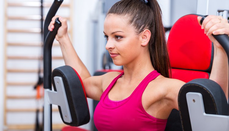 Young, adorable, cute, sexy trainer girl doing her butterfly chest workout exercise on the Pec Deck expressing power and strength in red sportswear.