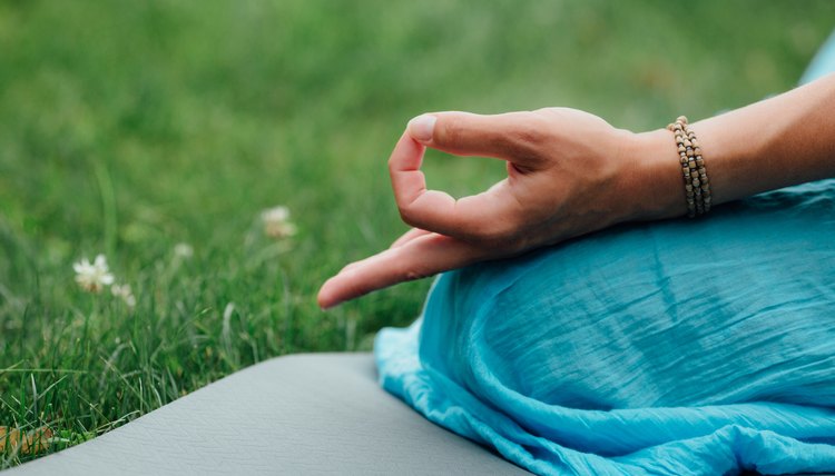 Woman meditating in the lotus position closeup. Hands close-up mudra. Sitting on a rug on the lawn of green grass on background