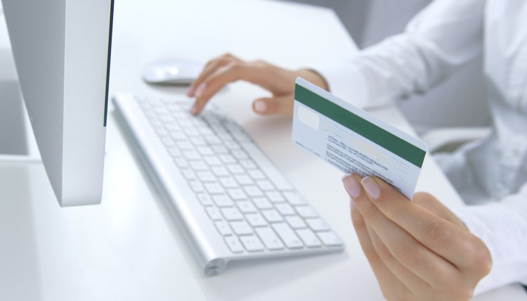 Una mujer frente a una computadora con una tarjeta de crédito en su mano.