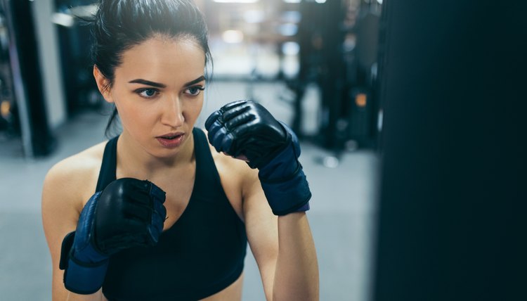 Side view of boxing attractive brunette woman punching a bag with kickboxing gloves in the gym workout. Sport, fitness, lifestyle and people concept.