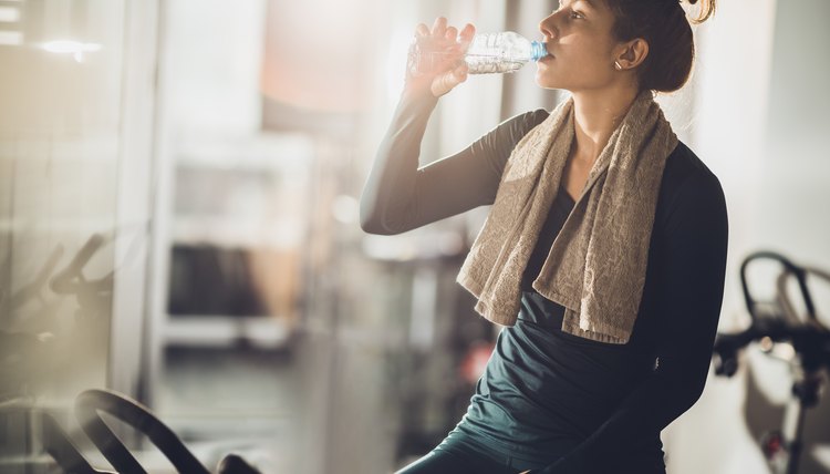 Thirsty athletic woman drinking fresh water on a break in a gym.