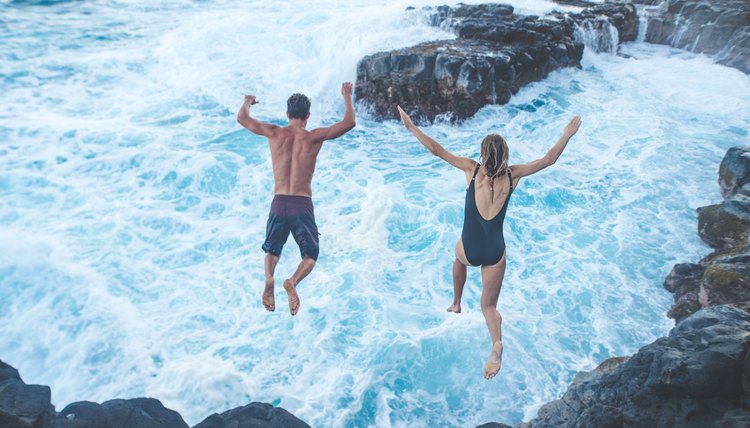 Beautiful couple jumping off cliff into ocean