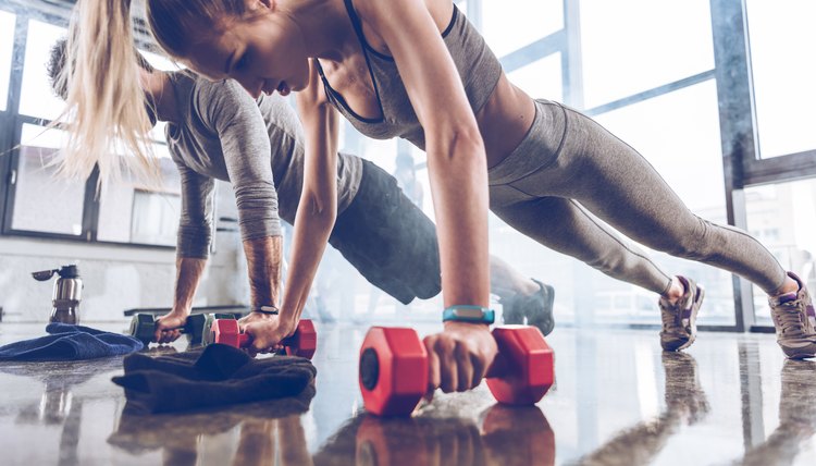 group of athletic young people in sportswear doing push ups with dumbbells at the gym, group fitness concept