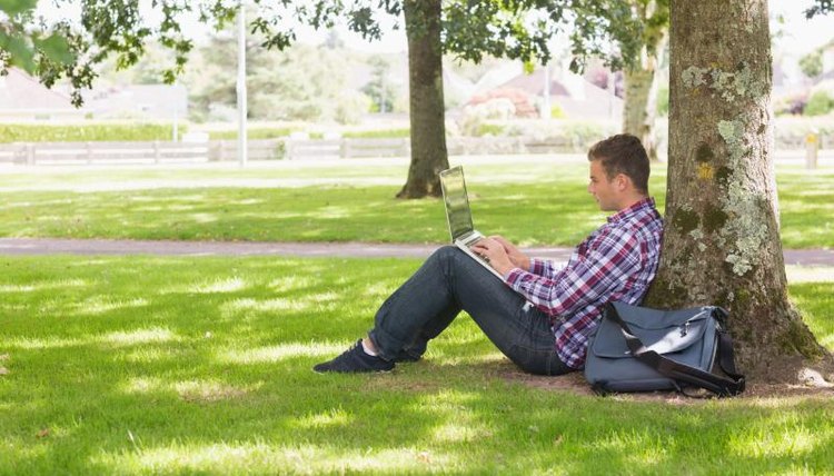 A college student working from his laptop outside.
