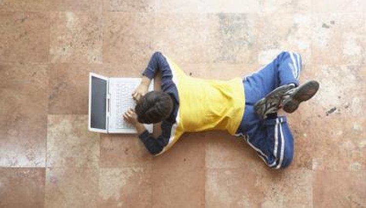 A high angle view of a boy looking at a laptop on the floor.
