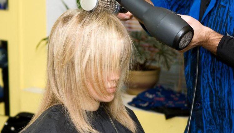 A woman in a salon is getting her hair blow dried.