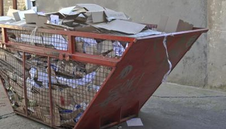 A large recycling receptacle on an urban sidewalk is filled with paper.