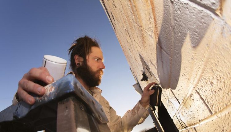 Male artist on ladder painting a wall.