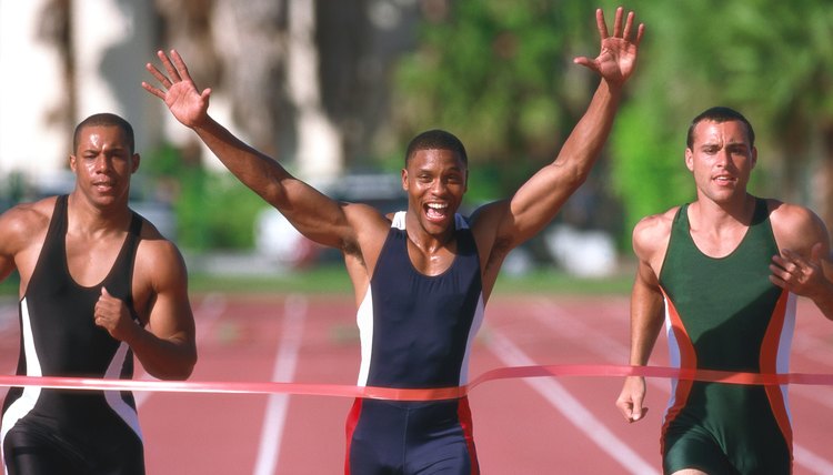 portrait of a young male athlete crossing the finish line first with his arms raised up in victory