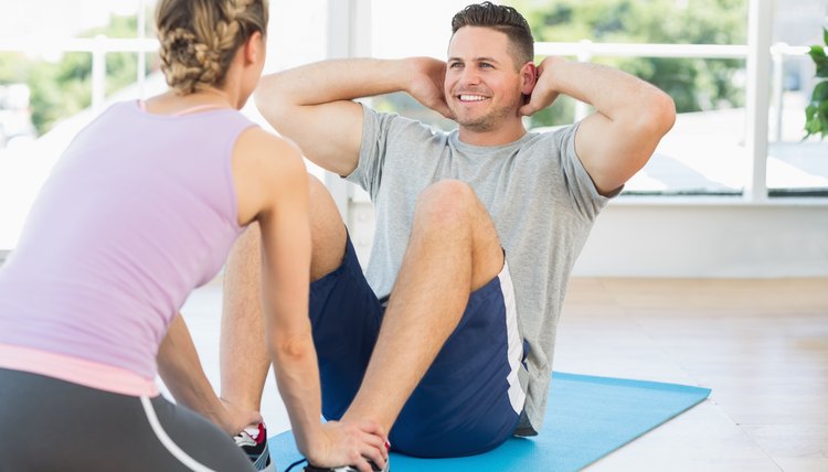 Trainer helping fit man in doing sits up