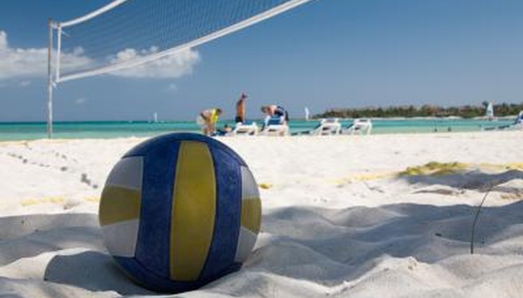 A volleyball in the sand underneath a net on the beach.