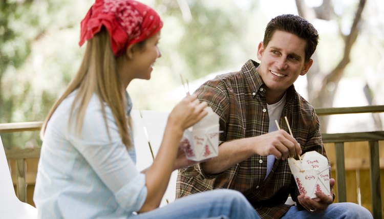 Cheerful young couple eating noodles on armchairs