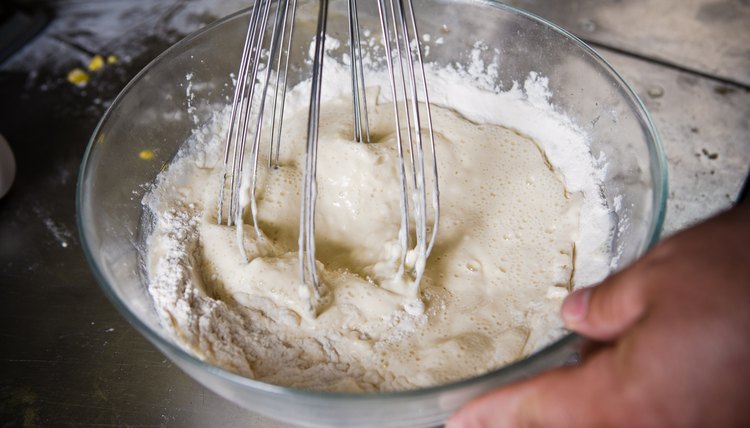 Baker beating eggs and flour in glass bowl