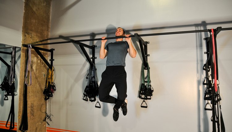 Man in a gym performing pull-ups on a pull-up bar.