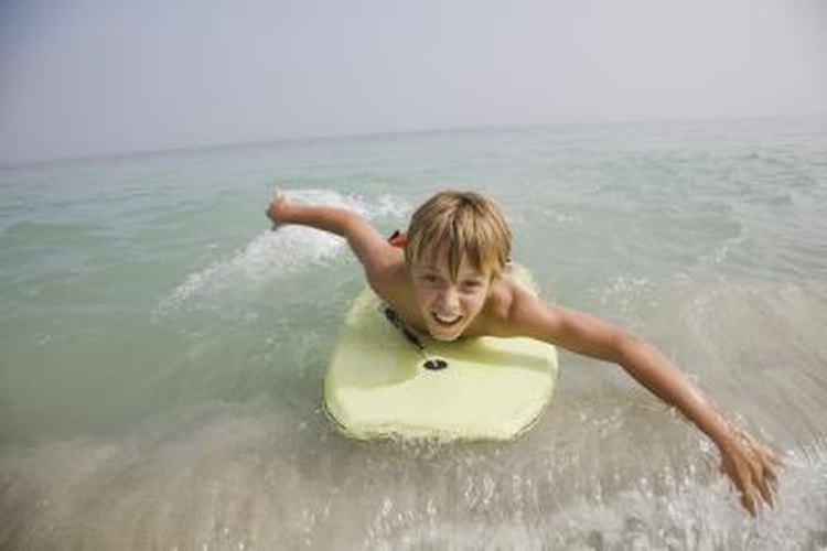 Jupiterimages/Goodshoot/Getty Images Rather than standing on the board, boogie boarders ride the waves while laying on their belly.